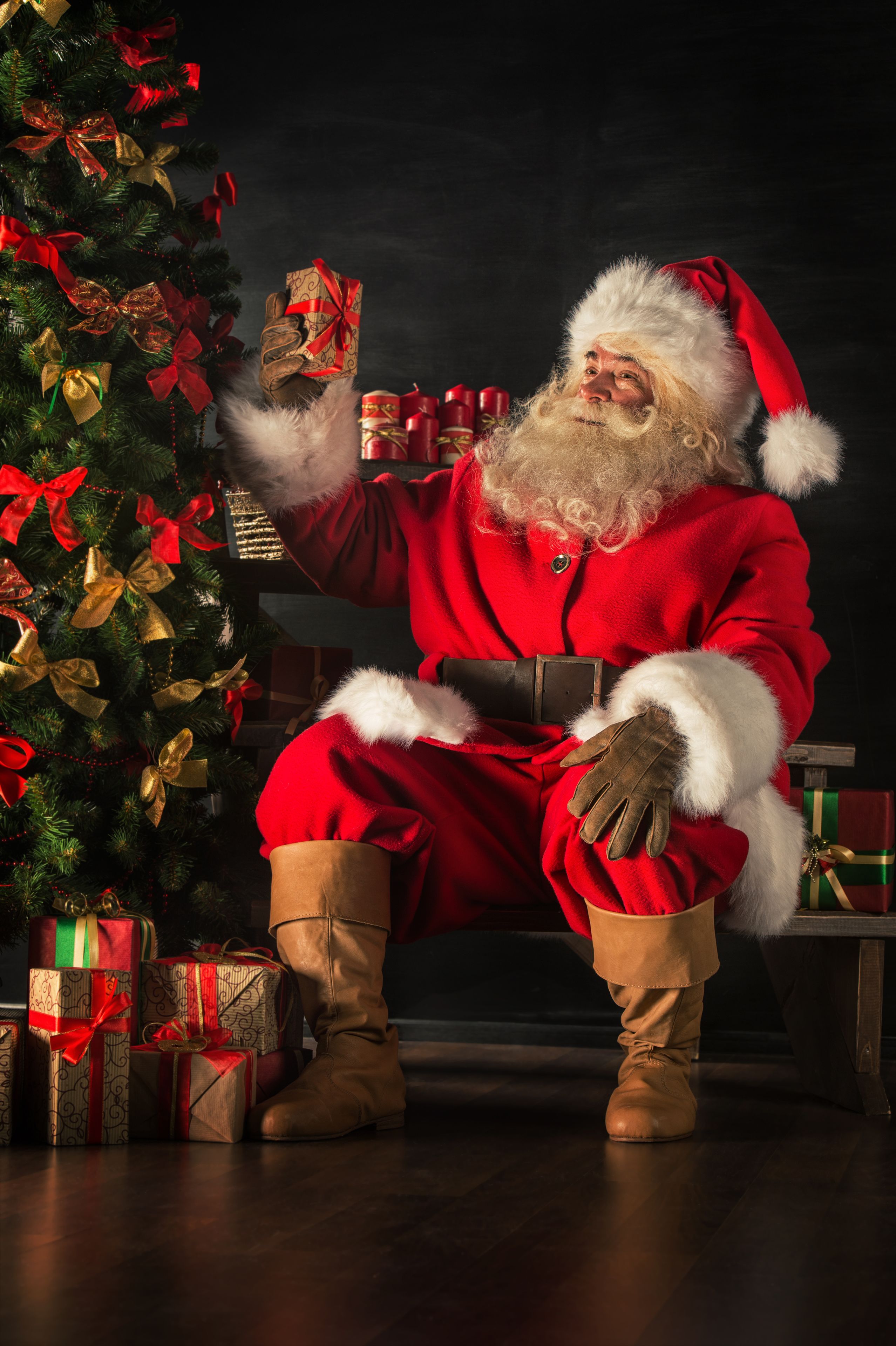 santa holding a gift next to the christmas tree